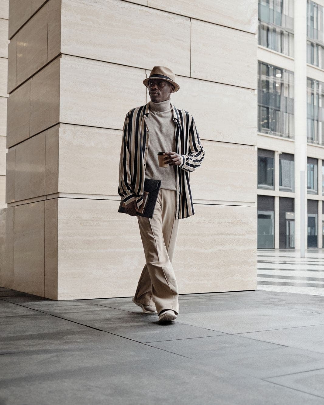 A man in a striped jacket and wide stone trousers walking past stone columns